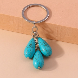 Ethic style turquoise teardrop keychain with silver metal rings on a warm aesthetic background