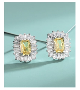 Detail of silver stud earrings featuring a rectangular yellow gemstone and clear accents