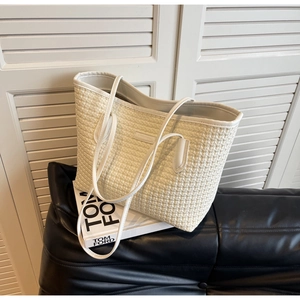 Detail of cream woven texture tote bag placed on a black surface with soft light