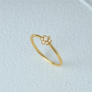 Macro shot of gold floral ring with sparkling zircon petals on white textured background