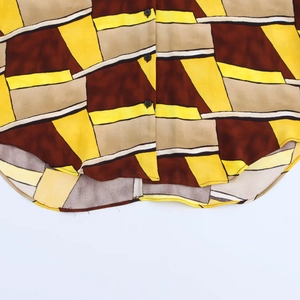 Dettaglio di camicia stampata con motivi geometrici marroni e orlo inferiore curvo