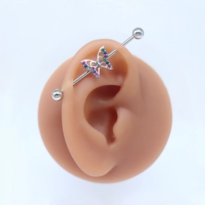 Detail view of a butterfly industrial barbell piercing with colorful rhinestones on a silicone ear model