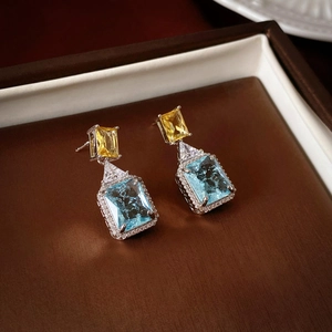 Close-up of geometric earrings with yellow, blue zircons and sparkling diamond halo