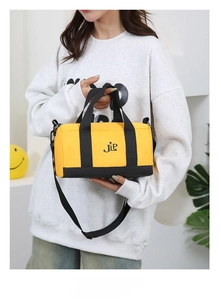 Detail of yellow nylon barrel bag with JLP embroidery, black handles and shoulder strap