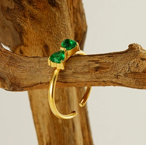 Détail de bague nœud dorée avec pierres vertes posée sur une branche en bois