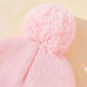 Dettaglio ravvicinato di un berretto in maglia rosa con un grande pompon morbido sopra