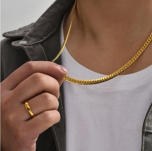 Close-up of a gold stainless steel flat curb chain necklace and ring on a model