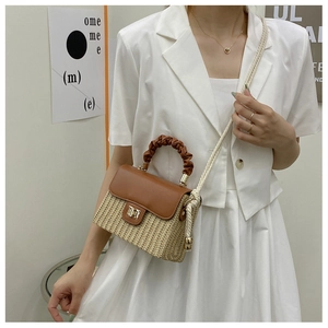 Detail of straw woven crossbody bag with brown leather flap and pleated handle on a model