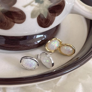 Macro detail of opal earrings in gold and silver finish resting on a ceramic saucer