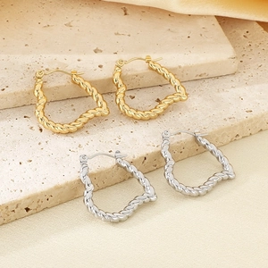 Detail view of twisted gold and silver hoop earrings on a textured stone display