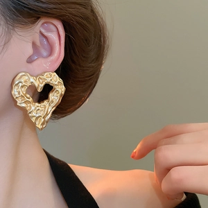 Detail of irregular gold heart earrings with textured lava-like metallic finish