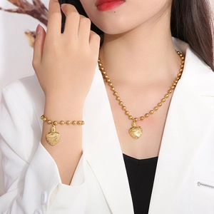 Detail of golden ball chain jewelry set featuring engraved heart locket pendants on model