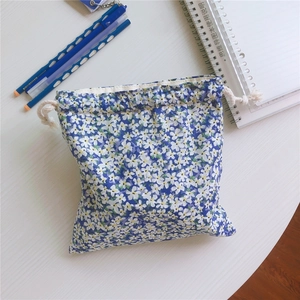 Detailed top view of blue floral cotton drawstring bag on white wood with stationery