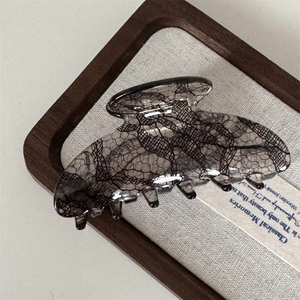 Detailed view of black lace pattern claw clip in a wooden tray with soft lighting
