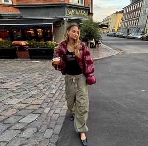Street style shot of a shiny burgundy cropped puffer jacket paired with olive cargo pants