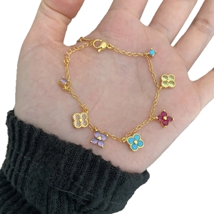 Bracelet trèfle doré avec breloques en zircon coloré tenu en main sur fond blanc