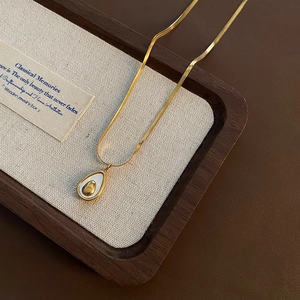 French shell pendant necklace in gold stainless steel on a wooden jewelry display case