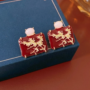 Macro detail of red enamel earrings with gold branch patterns on a blue jewelry box