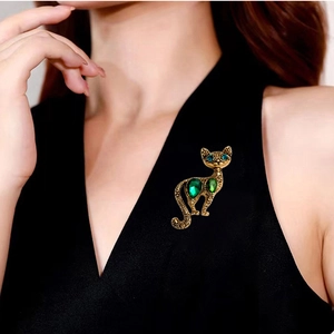 Close-up of vintage gold cat brooch with green crystals worn on black V-neck clothing