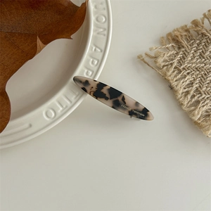 Detail of a handmade leopard print resin hair clip on a decorative white ceramic plate