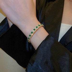 Double-row emerald and diamond geometric gold bangle worn on a model's wrist