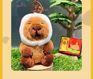 Detail of plush capybara keychain with white fuzzy hood and decorative bell on a wooden base