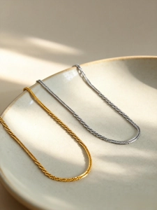 Detailed view of gold and silver sparkling twisted chain necklaces on a ceramic plate