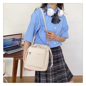 Detail of a beige nylon drawstring shoulder bag with a front zipper pocket in a student scene