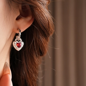 Close-up of a silver heart earring with a red gemstone and vintage patterns on a model