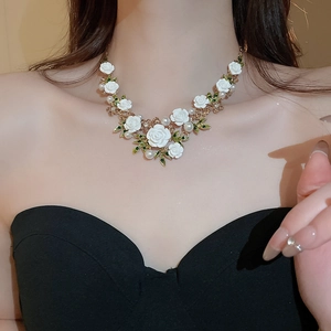 Detailed view of floral necklace with white roses, green leaves and pearls on gold chain