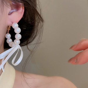 Macro view of elegant pearl hoop earrings featuring a delicate white ribbon bow detail