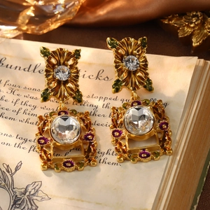 Detail of vintage gold-plated earrings with purple flowers and clear crystals on a book