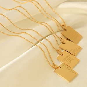 Four gold square inspirational pendant necklaces with bead chains on white silk background