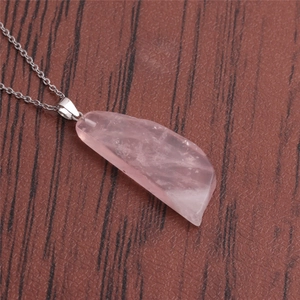 Détail d'un pendentif irrégulier en quartz rose avec chaîne argentée sur fond de bois