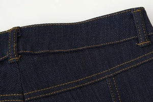 Détail de la taille d'un jean bleu foncé avec surpiqûres orange et passants de ceinture