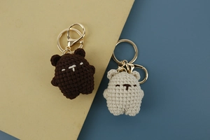 Detailed close-up of handmade knit bear keychains in brown and beige with gold hooks