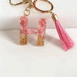Close-up of resin letter H keychain with pink flakes, gold sequins and silk tassel