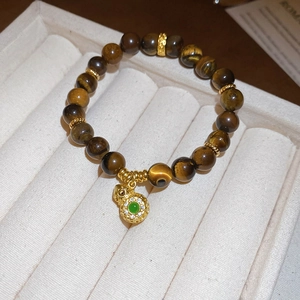 Detailed close-up of tiger eye bead bracelet featuring a gold gourd charm with green gem