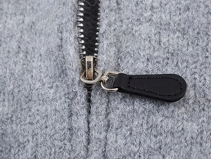 Detailed macro view of high-quality silver metal zipper with black leather puller on cardigan