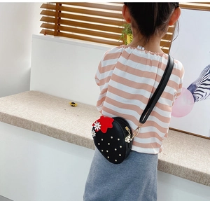 Kid's strawberry crossbody bag featuring white floral accents and golden studs worn on back