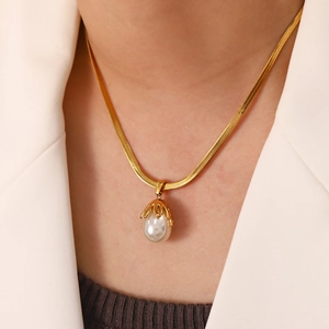 Elegant gold snake chain necklace with baroque freshwater pearl pendant on a white blazer