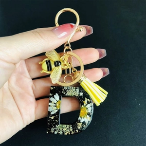Detail of Letter D resin keychain with real dried flowers, gold bee charm and yellow tassel
