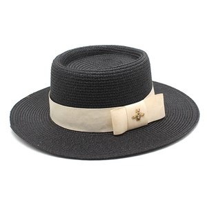 Detail of black straw boater hat featuring a woven texture and golden bee metal ornament