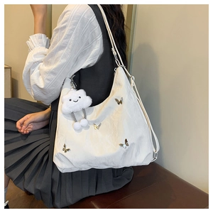 Detail of white nylon tote bag with metal butterfly charm and plush cloud pendant