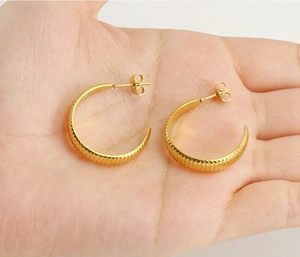 Vue macro de boucles d'oreilles créoles C en acier doré avec texture nervurée