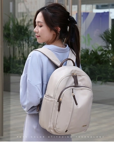 Detalle de mochila de nailon beige con asas de cuero marrón llevada por una modelo al aire libre