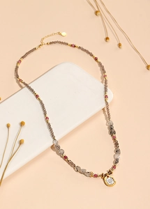 Detail view of multi-strand crystal bead necklace with gold square tag on beige tray