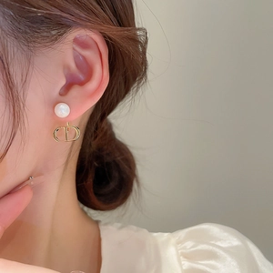 Close-up of model wearing gold D-letter earrings with a white faux pearl pendant