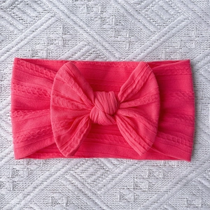 Detail of bright pink cable knit baby headband featuring a large soft decorative bow