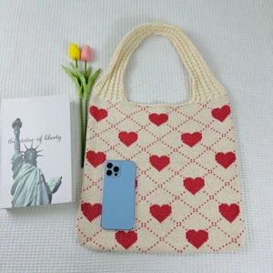Detail of beige knit tote bag with red heart pattern alongside tulips and books
